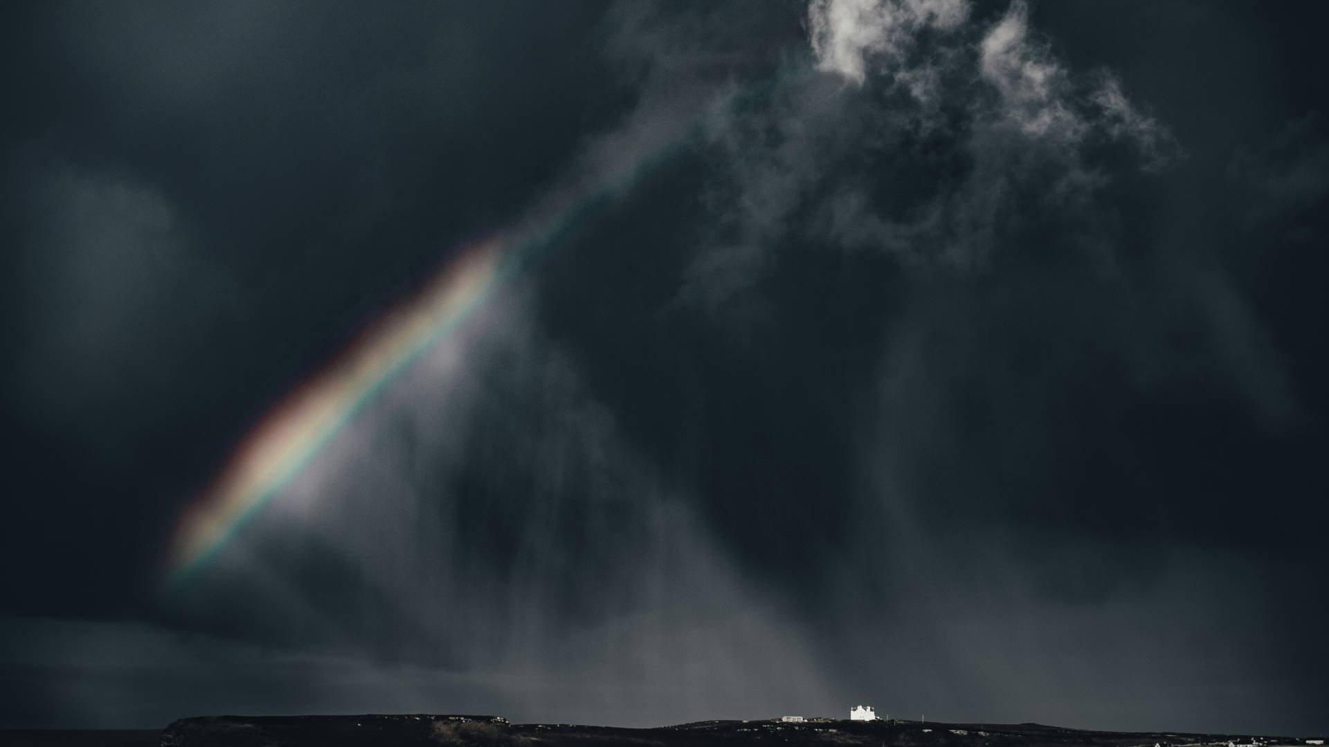 Photo of city under dark cloud and a rainbow