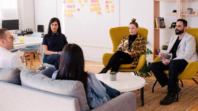 A group discussion with people on sofas and chairs with post its in background