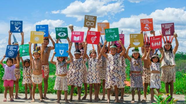 Indigenous children holding Sustainable Development Goals cards over their heads.